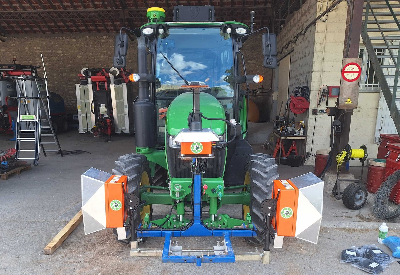 Tracteur vigneron vu de face dans un hangar, avec un module de caméra et d'éclairage Cropsy monté de chaque côté du châssis avant universel
