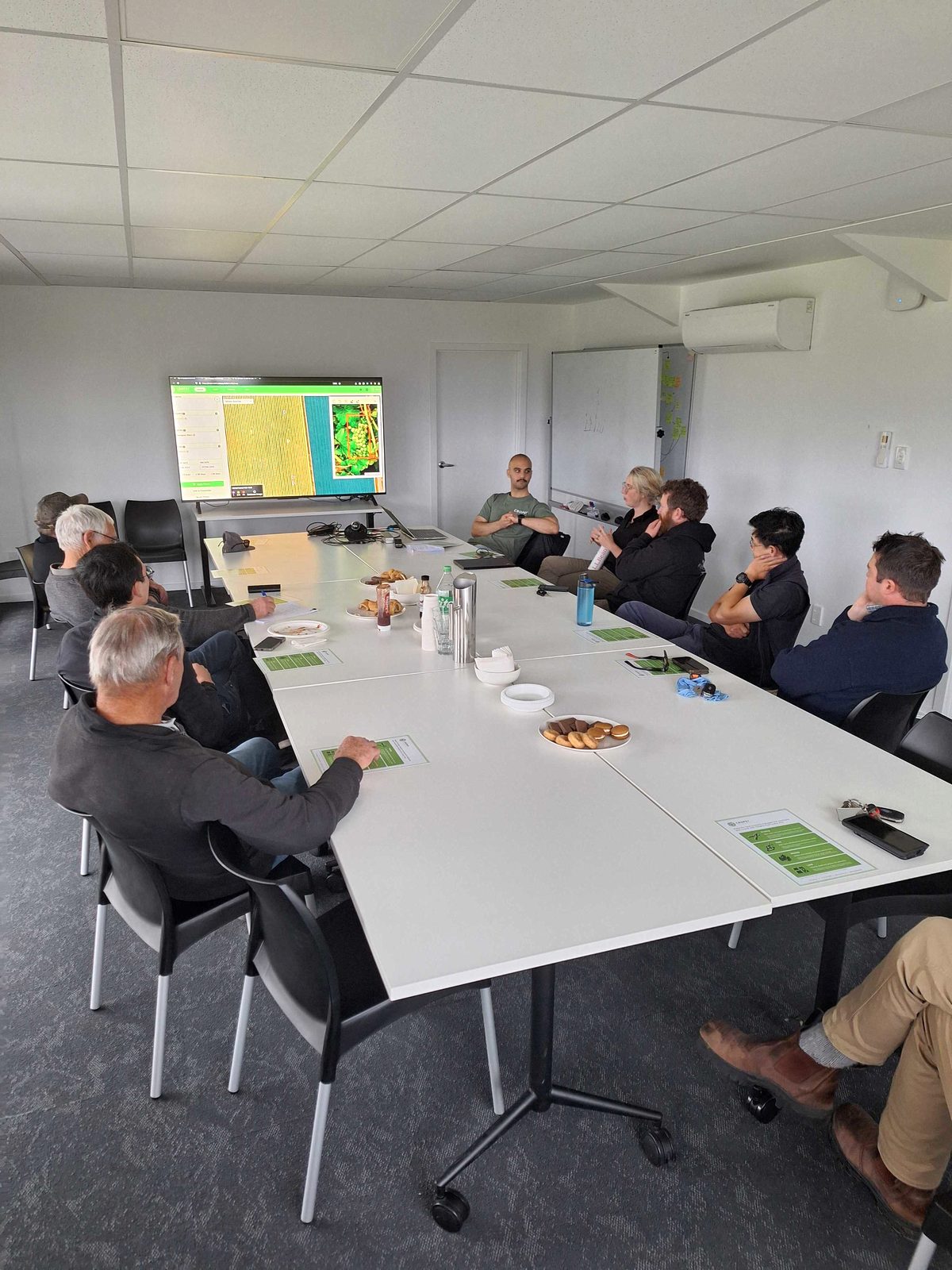 Une douzaine de viticulteurs autour d'une grande table regardent une carte de vignoble et des graphiques Cropsy projetés au mur