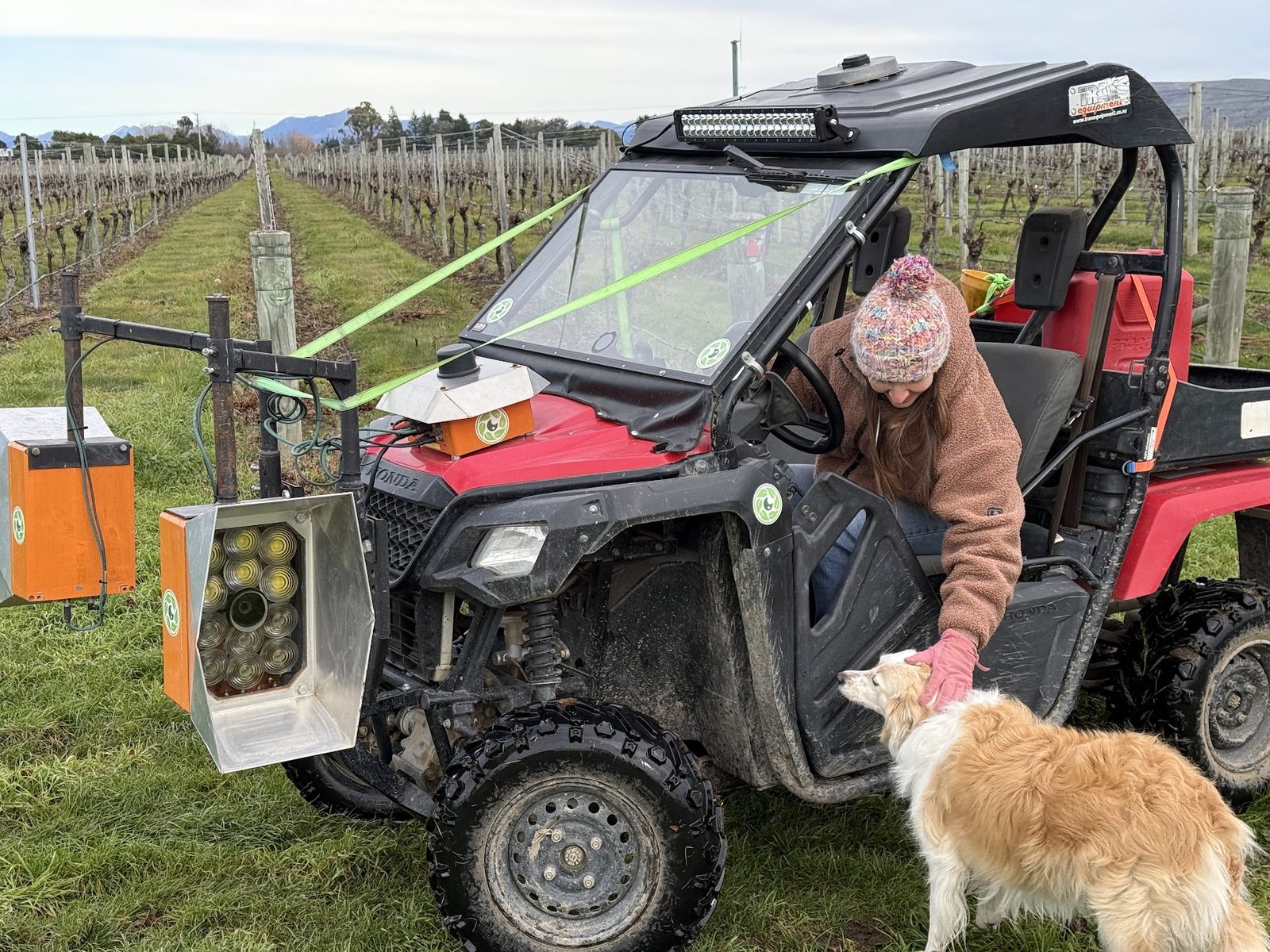 A grower leaning on a red buggy fitted with Cropsy scanner units, a farm dog beside the wheel