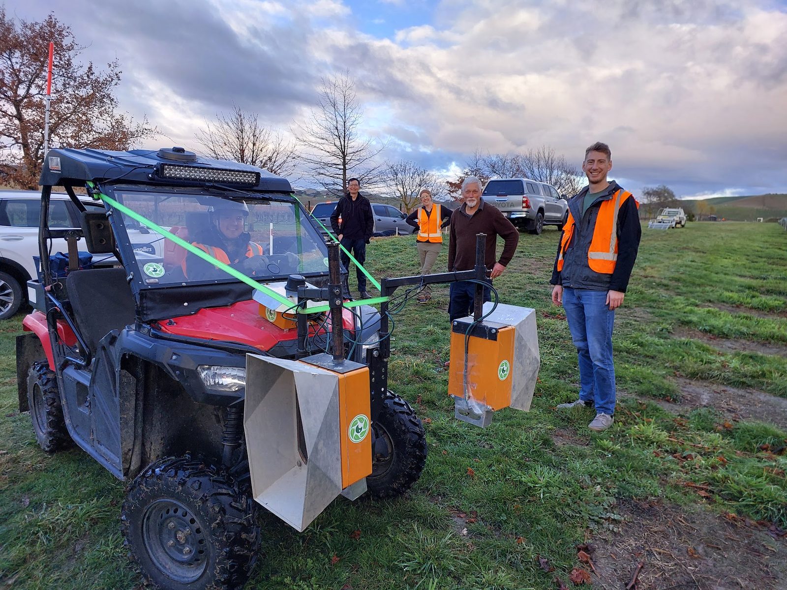 A red side-by-side buggy carrying Cropsy scanner units and white calibration targets, three of the team beside it in a winter vineyard