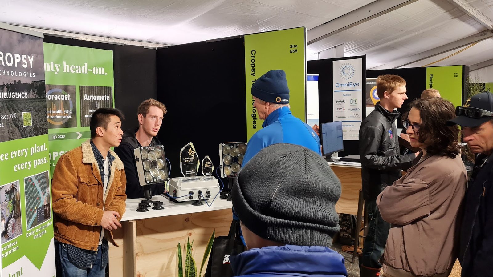 Visitors at the Cropsy stand at Fieldays, scanner units on the counter beneath green Cropsy banners