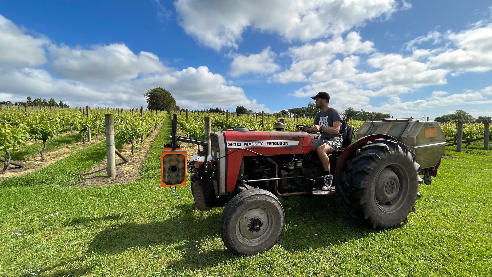 A red Massey Ferguson tractor with a front-mounted orange Cropsy scanner driving between vine rows