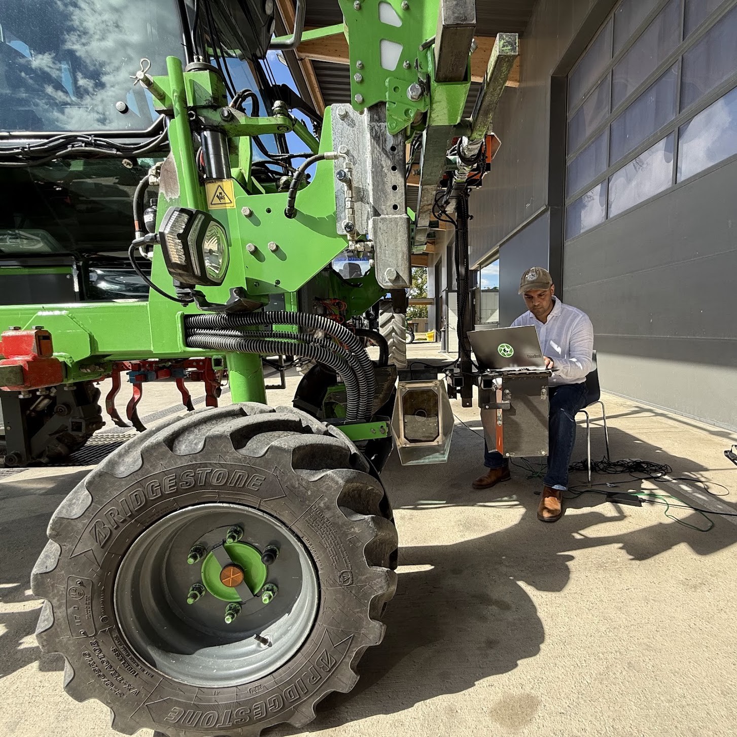 Cropsy scanner units and their stainless mounts fitted to a green straddle tractor, a team member at a laptop alongside working through the install