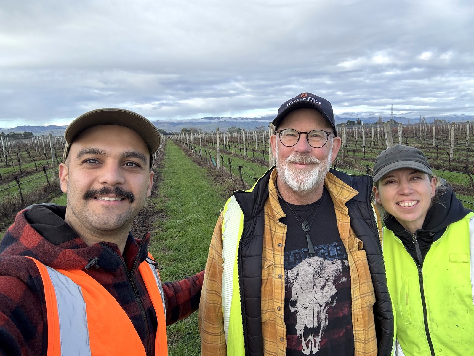 A Cropsy team member and two vineyard staff in a pruned winter vineyard, snow-dusted hills behind them