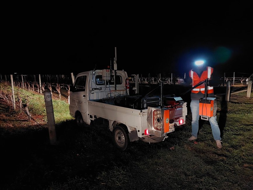 A white utility parked in a vineyard at night, its Cropsy scanner units lit by their own LED arrays
