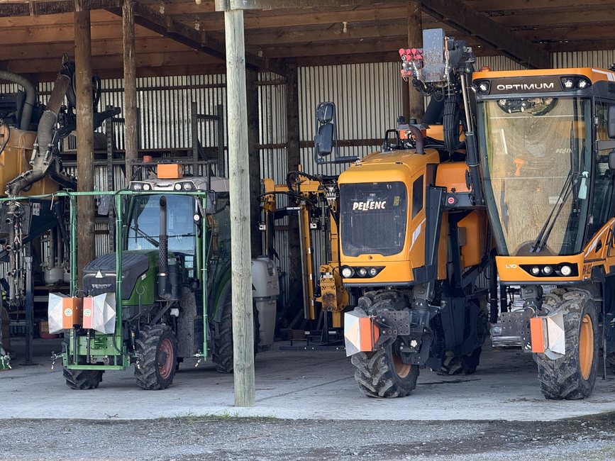 A green Fendt vineyard tractor and a yellow Pellenc harvester in a shed, both carrying Cropsy scanner units